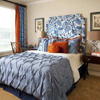 A stylish bedroom featuring a blue and white floral headboard, complemented by matching curtains and bedding. The room has decorative pillows that add a pop of orange for contrast.
