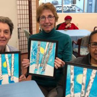 A group of women proudly display their artwork during an art class.