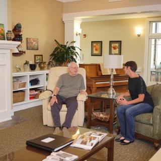A warm indoor setting with an elderly man and a younger person engaged in conversation.