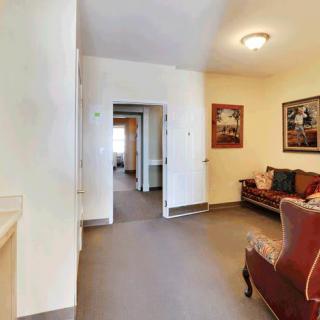 A cozy living room with a sofa and armchair, adorned with paintings on the walls, leading to an open hallway.