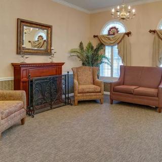A traditional living room with cozy seating around a fireplace, featuring armchairs, a sofa, and a chandelier.