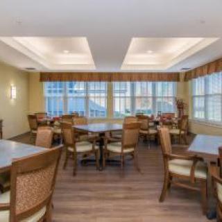 A spacious dining area with several tables and chairs, featuring large windows and wooden flooring.
