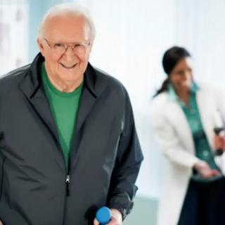 An elderly man smiling while exercising with dumbbells in a healthcare setting.