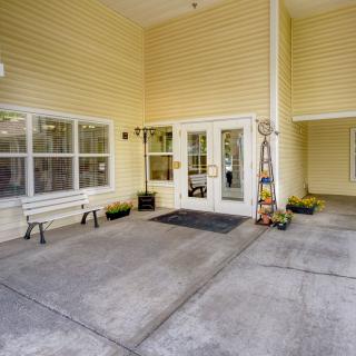 The entrance of a building with glass doors, yellow siding, and a bench.