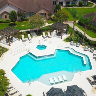 Aerial view of an outdoor swimming pool surrounded by lounge chairs and lush greenery in a residential area.