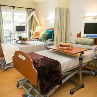 A modern hospital room with two patient beds, each equipped with bedside tables and privacy curtains.