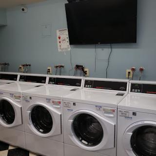 A row of modern washing machines in a laundromat, with a television mounted on the wall.