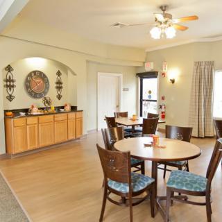 A cozy dining area with round tables and cushioned chairs, featuring a decorative wall and ceiling fan.