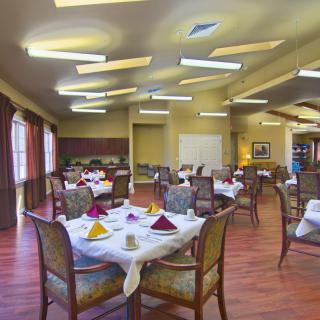 An elegantly set dining room with neatly arranged tables and chairs, featuring folded napkins and wooden floors.