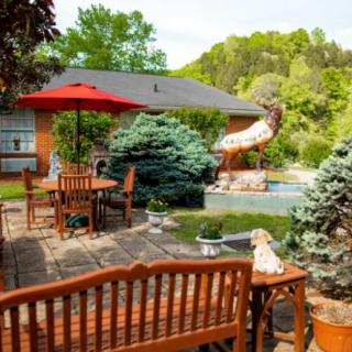 A cozy backyard patio with wooden furniture and a red umbrella, surrounded by lush greenery.