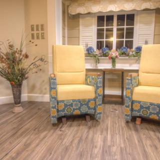 A cozy living room setting featuring two yellow upholstered chairs and a flower arrangement on a wooden floor.