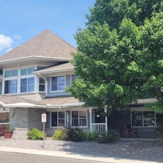 A charming residential building with a sloped roof and a large tree in front.