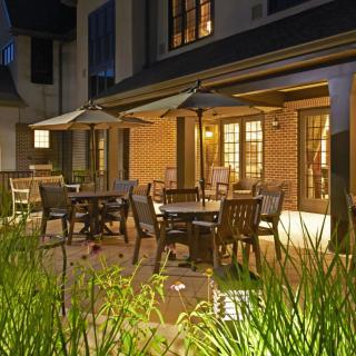 A cozy patio with tables and chairs under umbrellas, illuminated in the evening light.