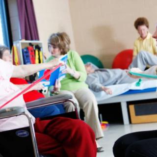 A group of elderly individuals participating in a therapy session, engaging in exercises with the assistance of healthcare professionals.