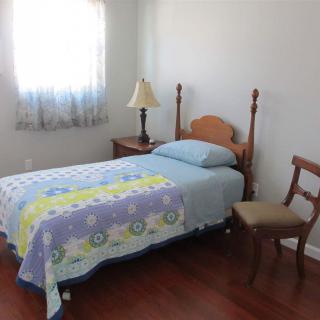 A simple bedroom with a single bed, nightstand and chair.