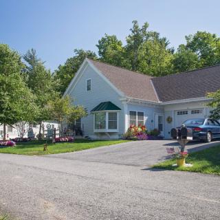 A suburban house with a driveway and a parked car, surrounded by trees and a well-kept lawn.