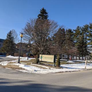 A peaceful winter scene featuring a sign surrounded by trees and snow under a clear blue sky.