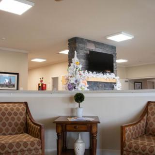 A modern interior seating area with comfortable chairs, a small table, floral decor, and a television mounted on the wall.