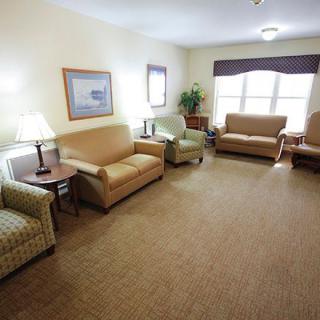 A cozy living room with multiple sofas and chairs arranged around a central carpeted area, complemented by lamps and windows.