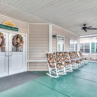 A welcoming porch with a row of floral-patterned rocking chairs and a 'Welcome Home' sign.