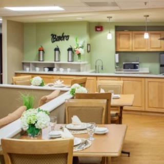 A cozy dining area with neatly set tables and a kitchen in the background.