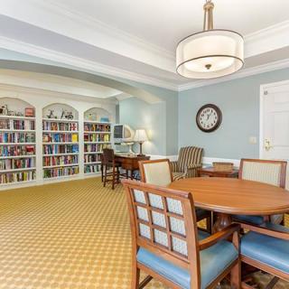 A cozy library room with bookshelves, a reading area, and a round table surrounded by chairs.