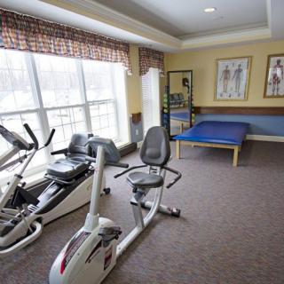 A therapy room equipped with stationary bikes and a treatment table, featuring large windows for natural light.