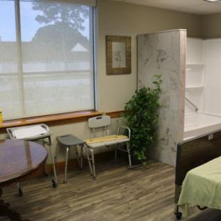 A well-lit hospital room with a bed, chairs, table, and a potted plant.