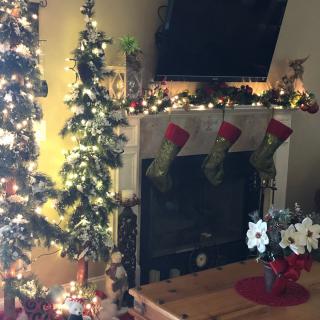 A cozy room decorated for Christmas with a lit tree, stockings over the fireplace, and festive lights.