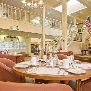 An elegant dining area with neatly set tables, surrounded by warm lighting and a grand staircase.