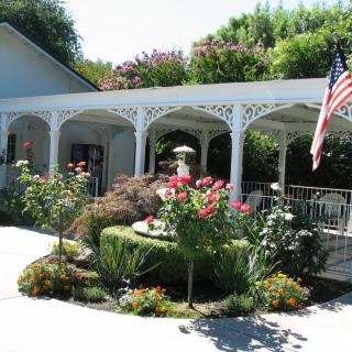 A charming garden with colorful flowers and a white veranda, adorned with an American flag.