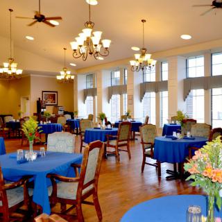 A well-lit dining room with tables covered in blue tablecloths and decorated with flowers.