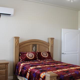 A cozy bedroom with a wooden bed and colorful bedding, featuring an air conditioner mounted on the wall.