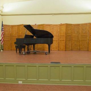 A grand piano on an empty stage in an auditorium.
