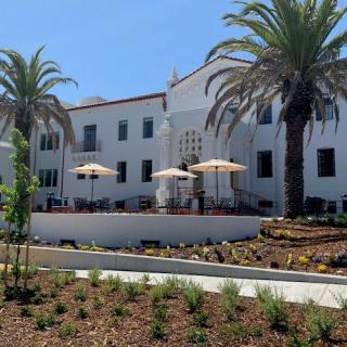 A sunny day view of a white building with palm trees and an outdoor seating area.