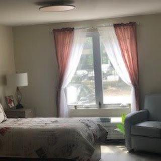 A cozy bedroom with sunlight streaming through a window adorned with pink and white curtains.