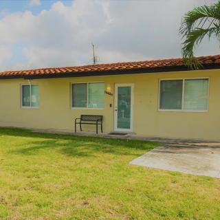 A small residential house with a tiled roof and a grassy lawn, featuring a palm tree.