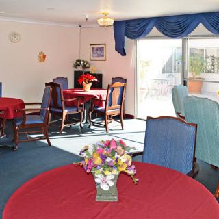 A cozy dining room with red tablecloths and blue chairs, featuring decorative flowers and ample natural light.
