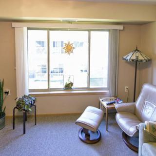 A cozy living room corner with a comfortable chair and footrest near a large window, accented by a lamp and greenery.