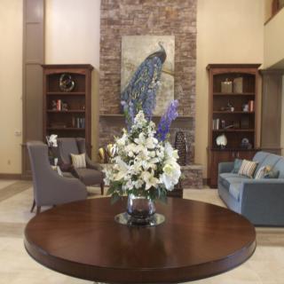 A beautifully decorated living room featuring a central table with a floral arrangement, surrounded by comfortable seating and adorned with a peacock artwork.