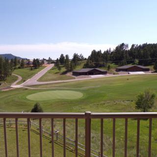A scenic view of a golf course surrounded by trees and buildings under a clear, sunny sky.