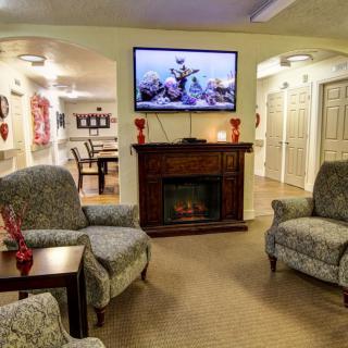 A cozy living room with comfortable armchairs and a fireplace, featuring a television mounted above.