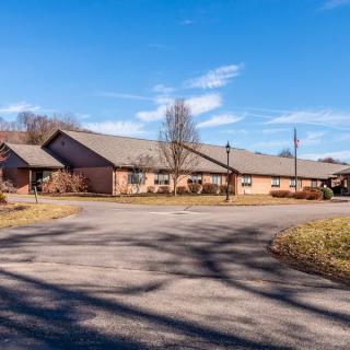 A wide view of a residential building with a driveway and trees under a clear blue sky.