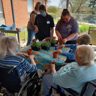 Seniors and caregivers enjoying a gardening activity, potting plants together in a sunny outdoor setting.