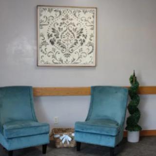 Two teal chairs in a waiting room setting with decorative artwork and a plant.