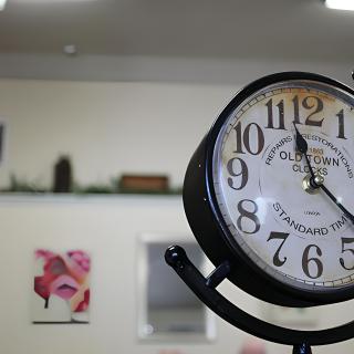 A vintage-style clock stands prominently in a cozy interior with wall art in the background.