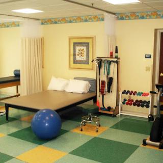 A well-equipped physical therapy room featuring exercise equipment, a bed, and a blue exercise ball.