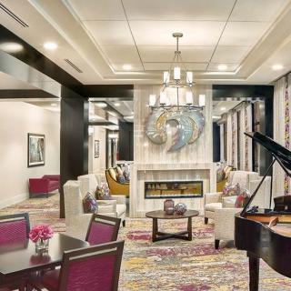 A luxurious and elegantly designed living room featuring a grand piano, chandelier, modern furniture, and a fireplace.