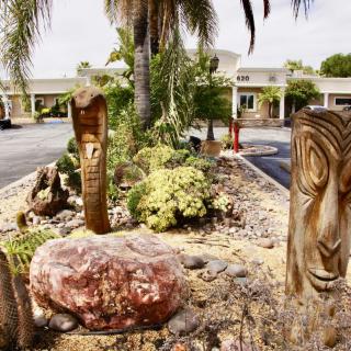 Tiki statues amidst a landscaped garden with palm trees and rocks.