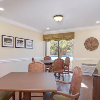 A cozy dining area with tables and chairs, decorated with wall art and natural light streaming through a window.